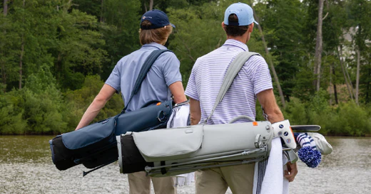 Two golfers standing side by side with their golf bags slung across their backs